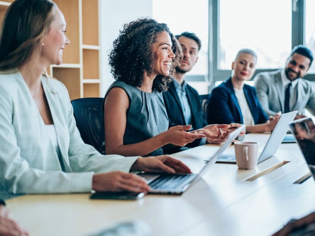 Diverse business professionals in a meeting, discussing ideas around a table with laptops.